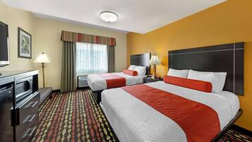 A hotel room with two beds, a desk, a TV, and a patterned carpet.