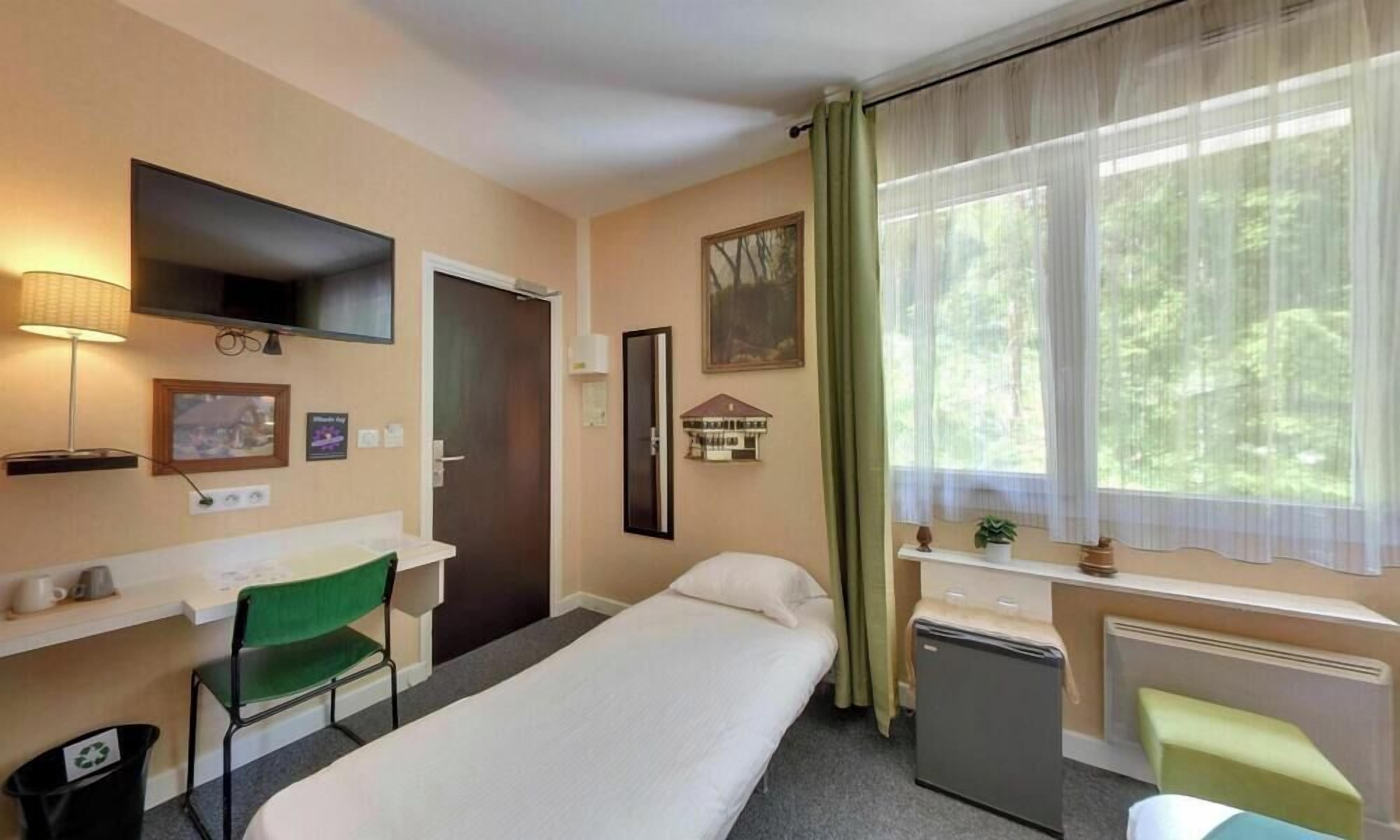 Une chambre d’hôtel équipée d’un lit, d’un bureau, d’une chaise, d’une télévision, d’une fenêtre avec des rideaux et d’un petit radiateur.