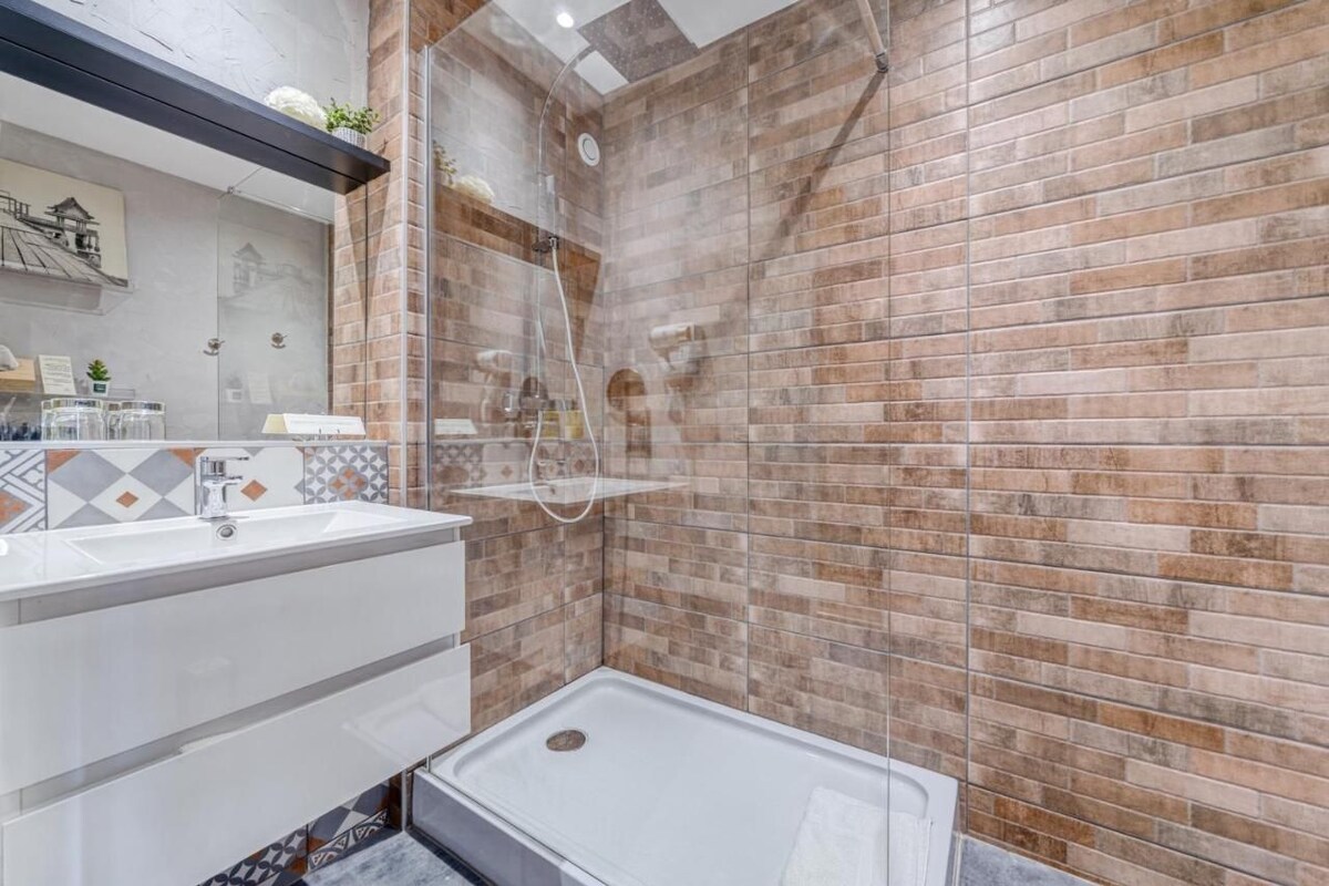 A modern bathroom with a glass-enclosed shower, a white sink, and a tiled wall.