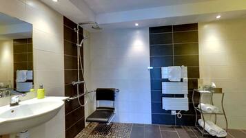 A modern bathroom with a large sink, a shower with a handheld showerhead, a bench, and a towel rack with towels.
