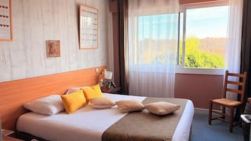 Hotelkamer met een groot bed, een houten hoofdeinde, een nachtkastje met een lamp, een stoel en een raam met uitzicht op bomen.