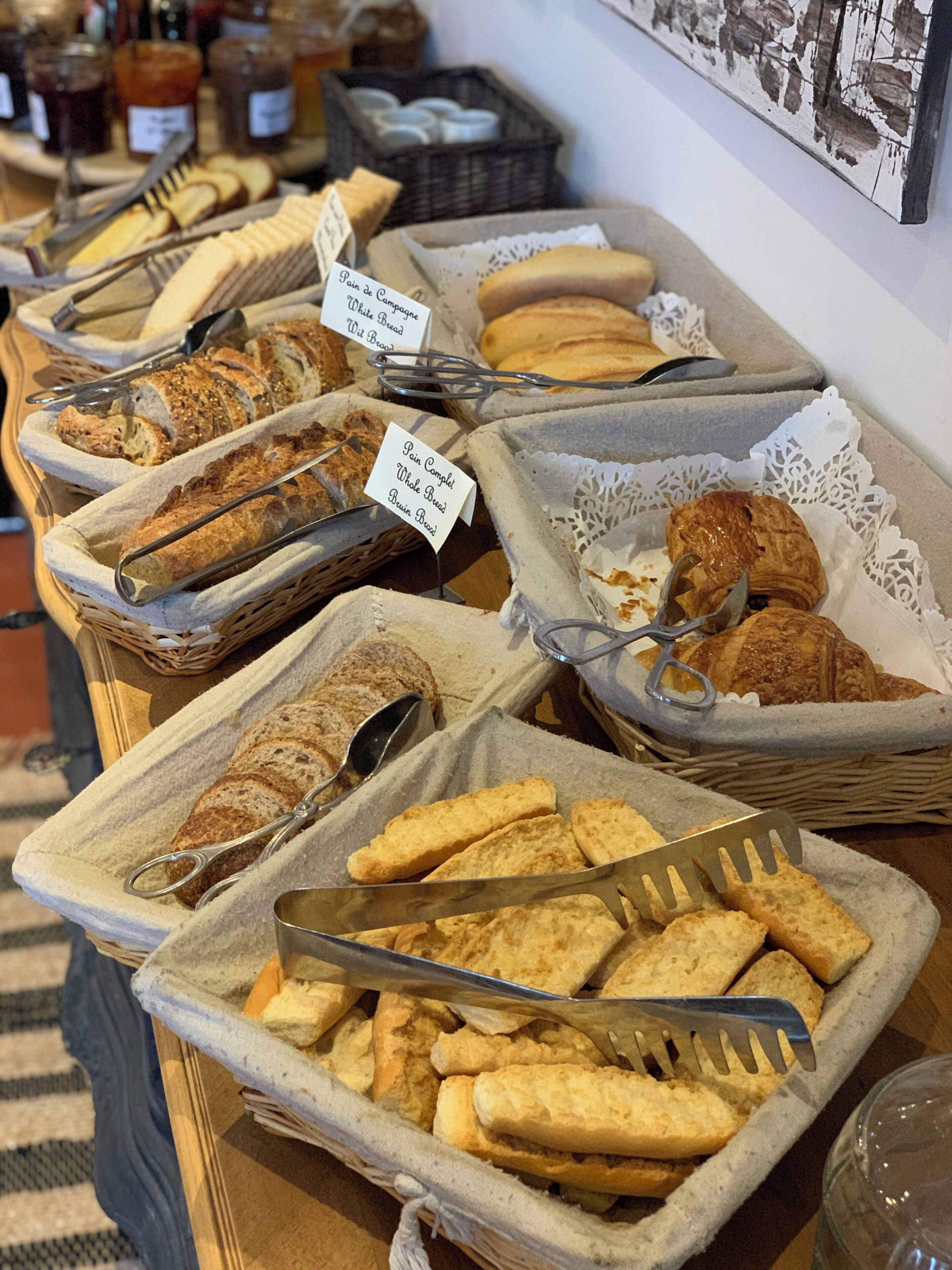 Variedad de panes y pasteles expuestos en cestas con etiquetas que indican diferentes tipos.