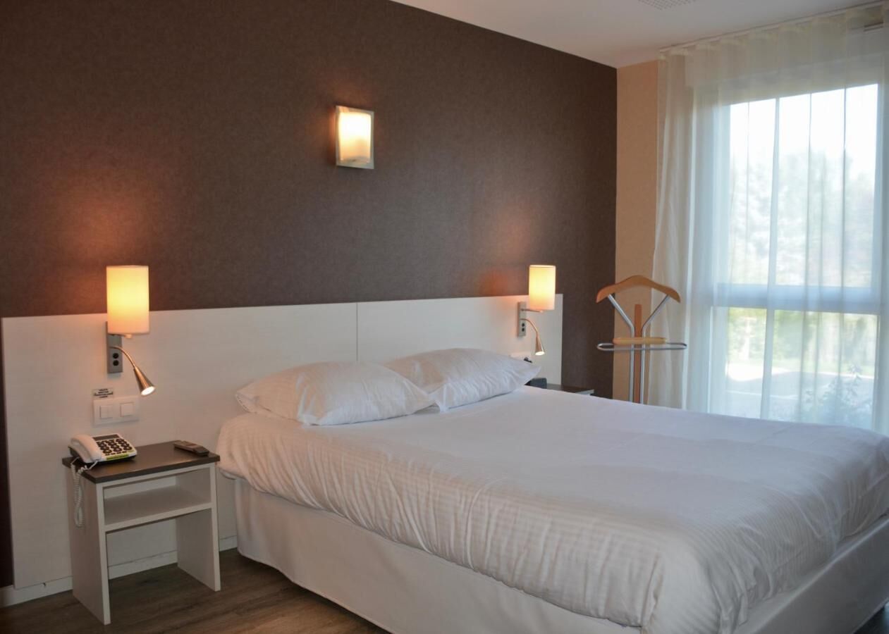 Et hotelværelse med en stor seng, to sengeborde med lamper og et vindue med lette gardiner.