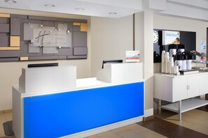 A hotel reception desk with a blue accent, a clock, and a coffee machine.