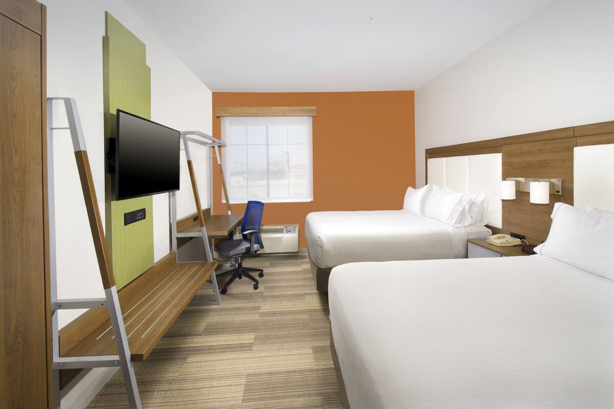 A hotel room with two beds, a desk with a chair, a television, and a window.