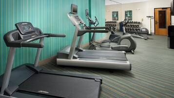 Un gimnasio con cintas de correr, elípticas y un televisor en la pared.