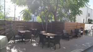 Un patio exterior con mesas y sillas de madera, rodeado por un cerco de madera y árboles.