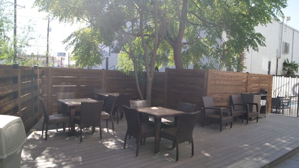An outdoor patio with wooden tables and chairs, surrounded by a wooden fence and trees. - Holiday Inn Express & Suites San Antonio-Dtwn Market Area by IHG (San Antonio)