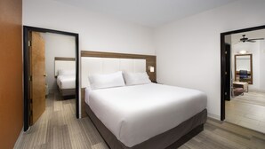 Habitación de hotel con una cama grande, cabecera de madera, mesita de noche, espejo y puerta que da a otra habitación.