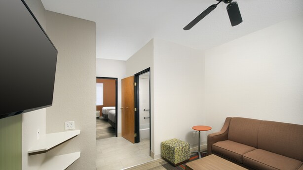 Una habitación de hotel moderna con una televisión de pantalla plana, un sofá, una pequeña mesa redonda y un ventilador de techo.
