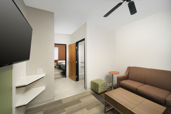 A modern hotel room with a flat-screen TV, a sofa, a small round table, and a ceiling fan. - Holiday Inn Express & Suites San Antonio-Dtwn Market Area by IHG (San Antonio)