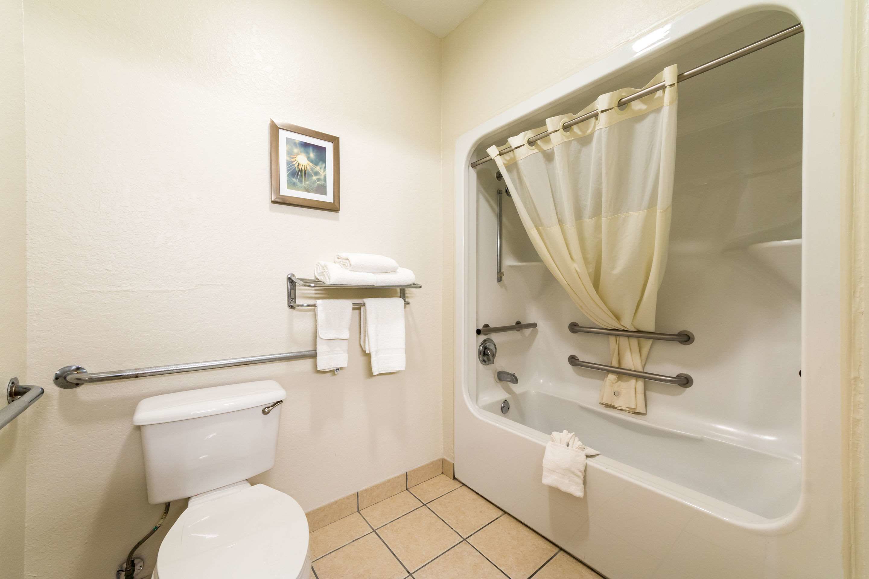 A bathroom with a toilet, a bathtub with a shower curtain, a grab bar, and a small shelf with towels.