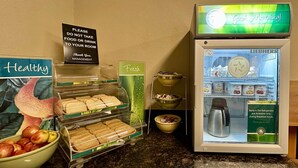 Een ontbijtbuffet met een bord waarop staat 'Gelieve geen eten of drinken mee naar uw kamer te nemen', een bord met de tekst 'Dank u, management' en een koelkast met borden waarop 'Goedemorgen!' en 'Producten in de koelkast zijn alleen verkrijgbaar tijdens de ontbijturen' staan.