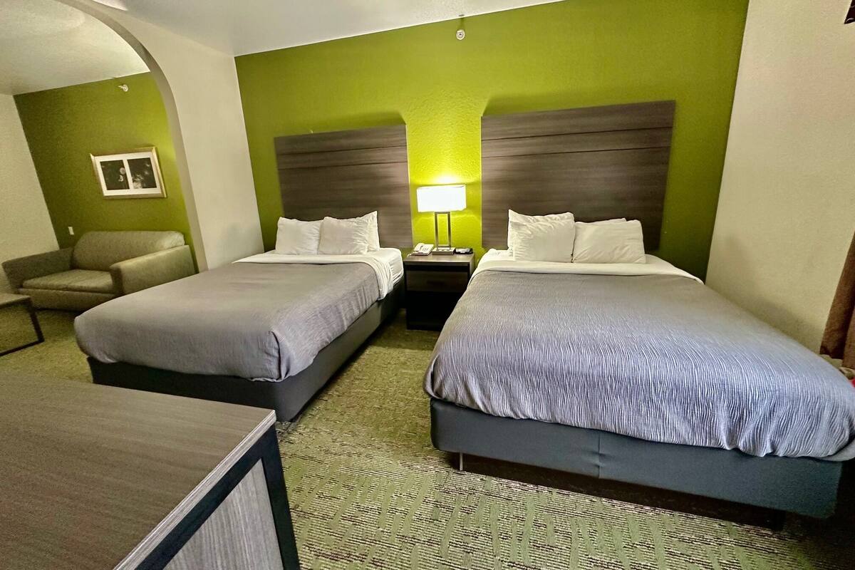 Een hotelkamer met twee bedden, een bureau, een stoel en een nachtkastje met een lamp.