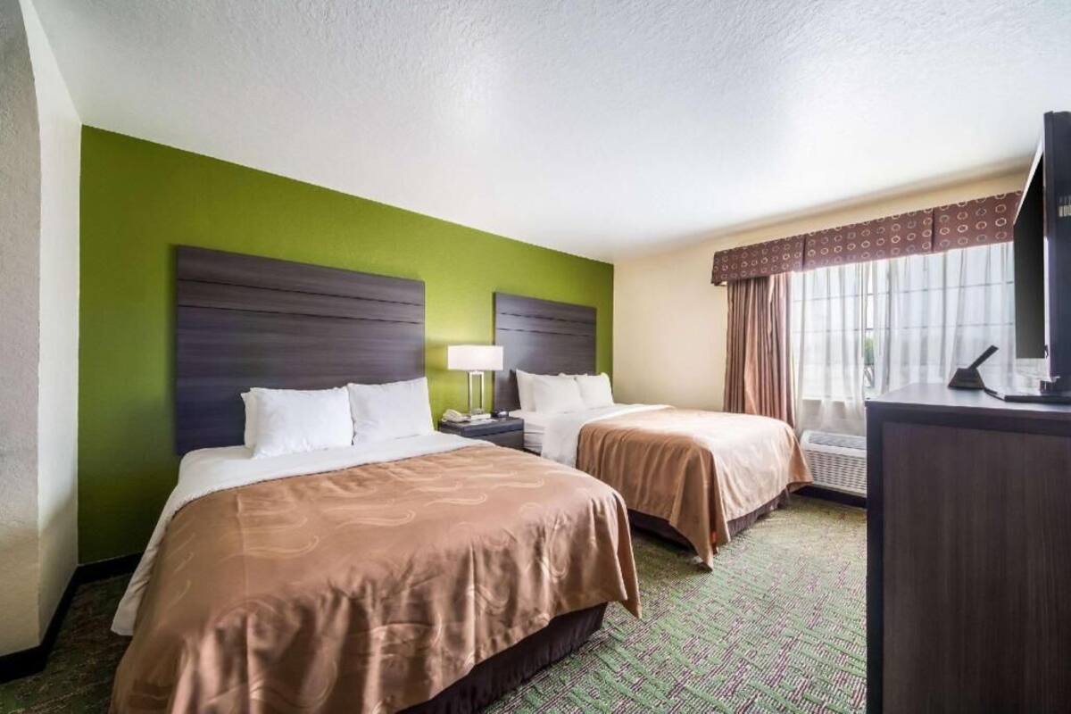 Een hotelkamer met twee bedden, een bureau, een stoel, een televisie en een raam met gordijnen.