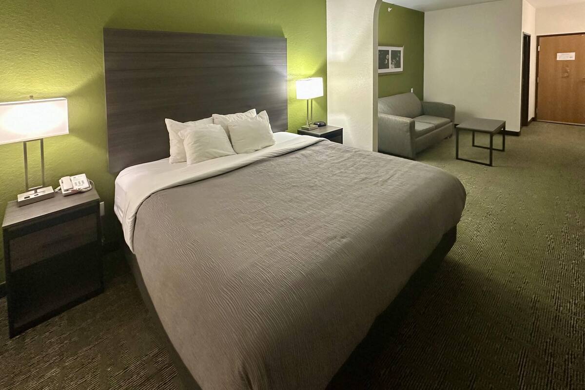 Een hotelkamer met een groot bed, een nachtkastje met een lamp, een klein tafeltje en een bank.