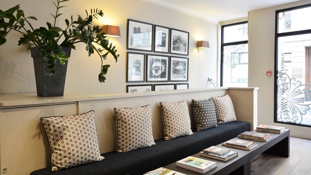 A modern interior with a black sofa, patterned cushions, a coffee table with books, a potted plant, and framed pictures on the wall. - Villa Des Princes (Paris)