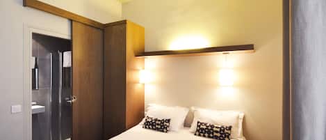 A hotel room with a bed, bedside lamps, a nightstand, a wooden wardrobe, and a shower area.