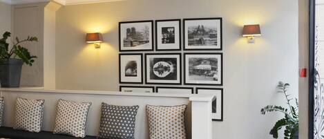 Een moderne woonkamer met een bank, gekleurde kussens, een salontafel met boeken en aan de muur hangende fotolijstjes.
