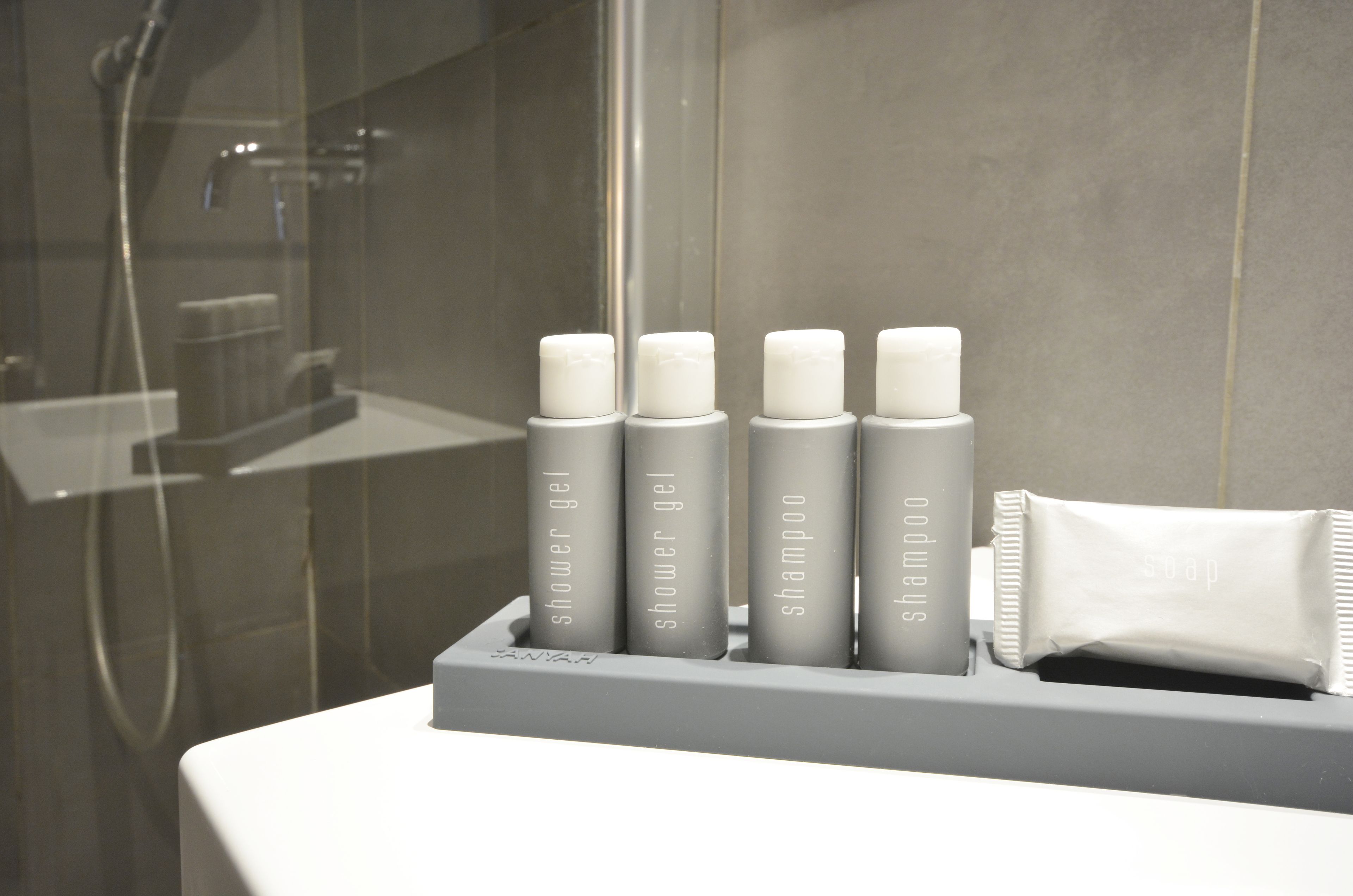 A bathroom with a shower area and a shelf holding toiletries including shower gel, shampoo, and soap.