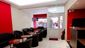 A hotel lobby with black leather sofas, small round tables, and a red accent wall. - Hotel St-Etienne (Lourdes)