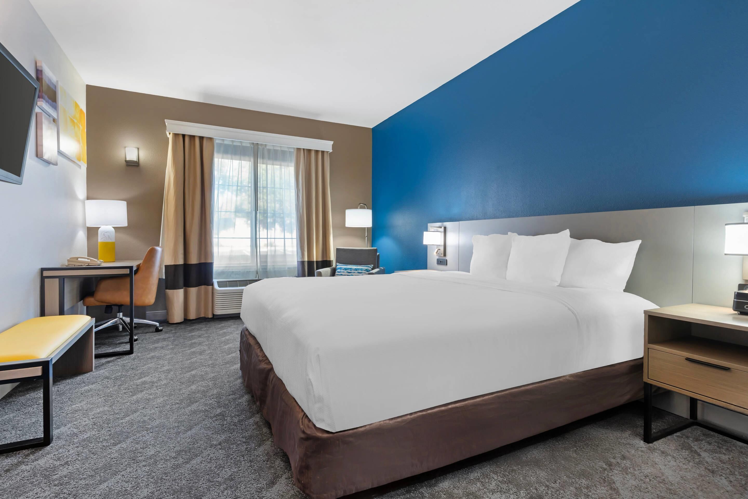 Une chambre d’hôtel avec un grand lit, un bureau, une chaise et une fenêtre avec des rideaux.
