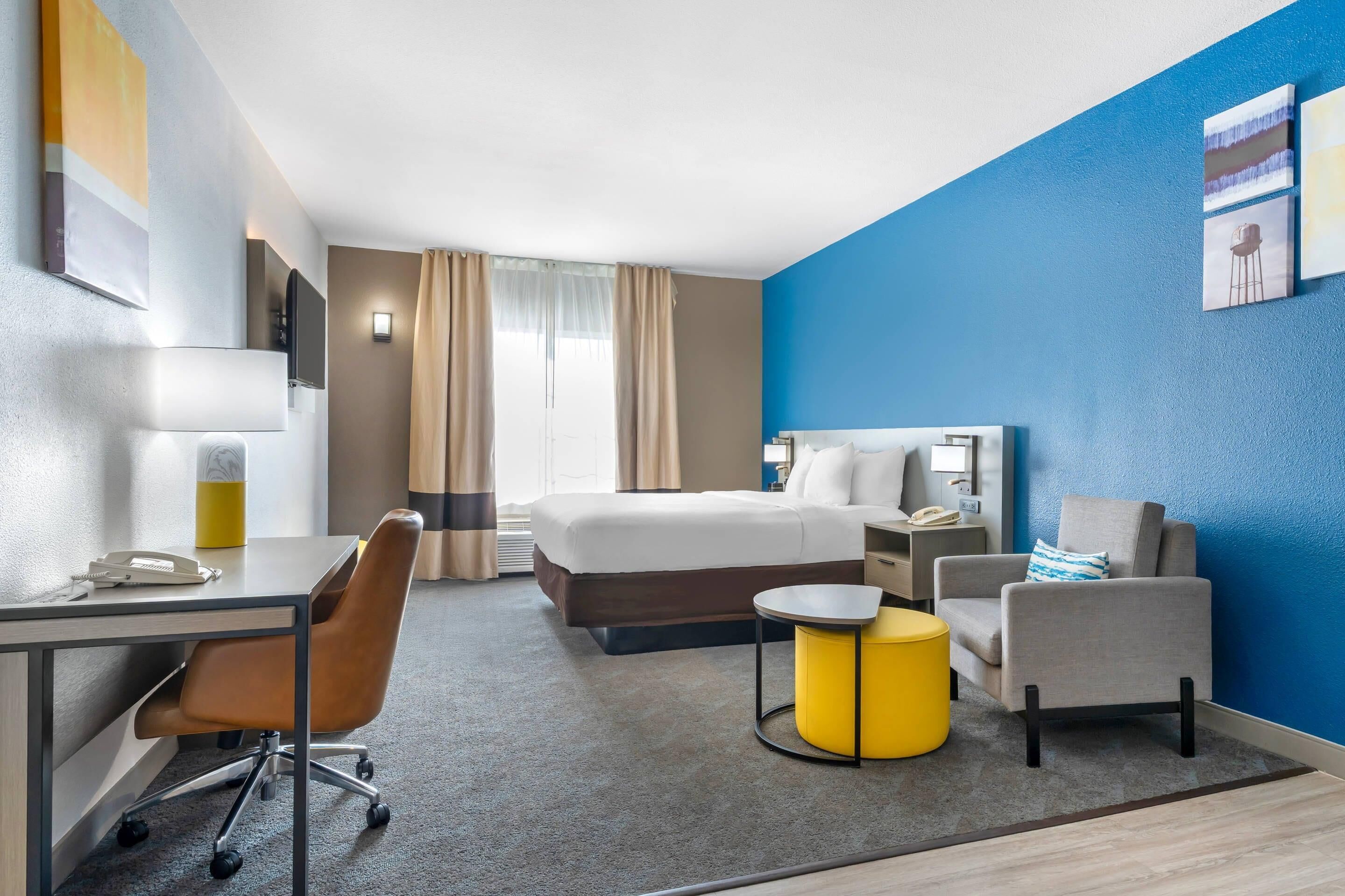 Habitación de hotel con cama, escritorio, silla y una mesita de noche con base amarilla.