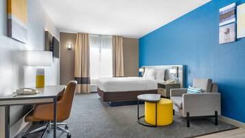 Habitación de hotel con cama, escritorio, silla y una mesita de noche con base amarilla.