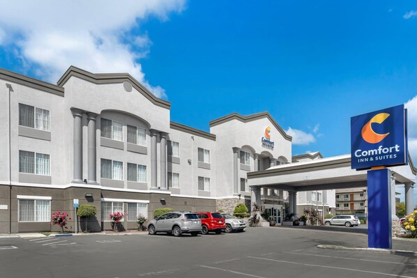 A Comfort Inn & Suites hotel with a parking lot, multiple vehicles, and a clear blue sky. - Comfort Inn & Suites Sacramento - University Area (Sacramento)
