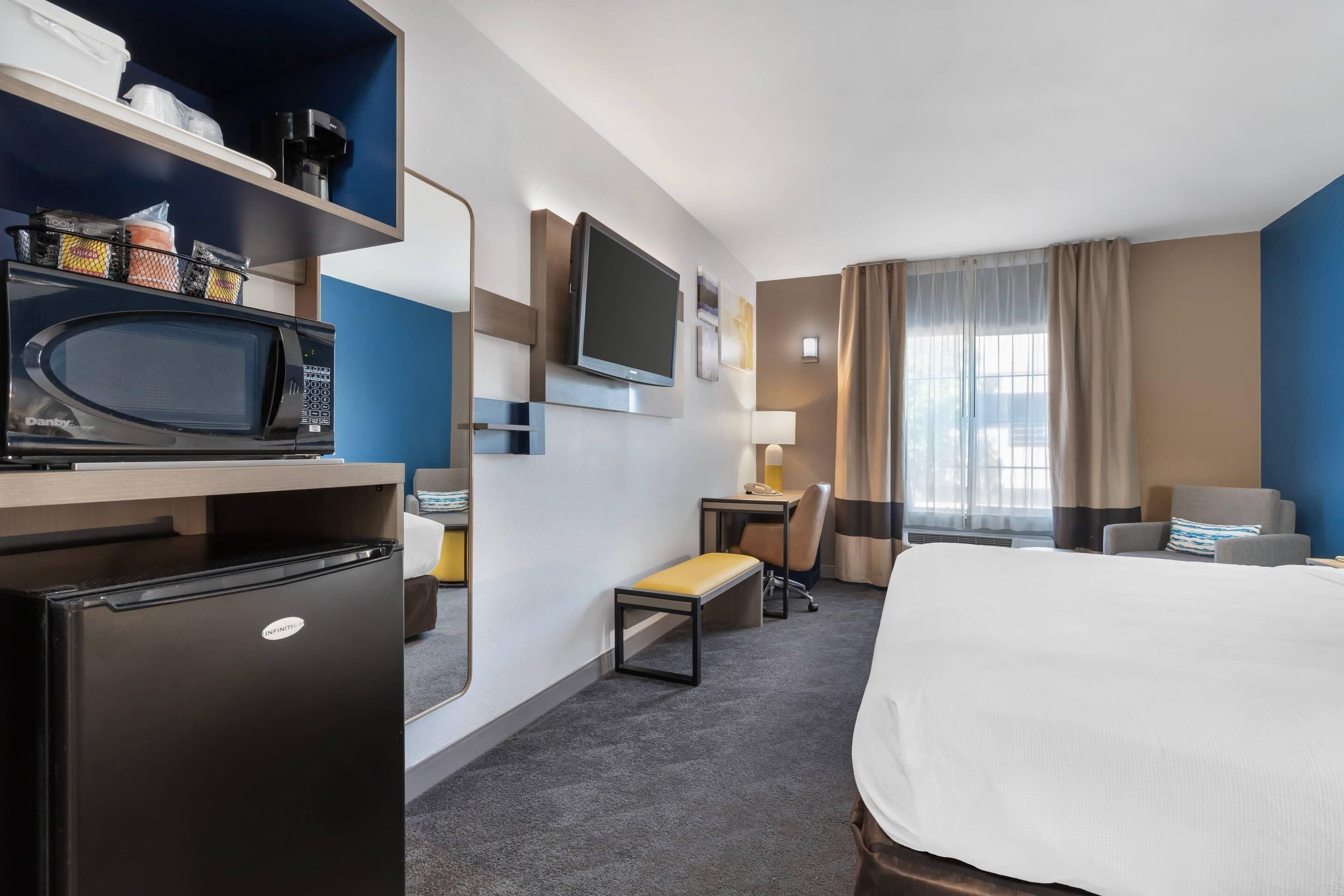 Habitación de hotel con cama, escritorio con silla, televisor, refrigerador y microondas.