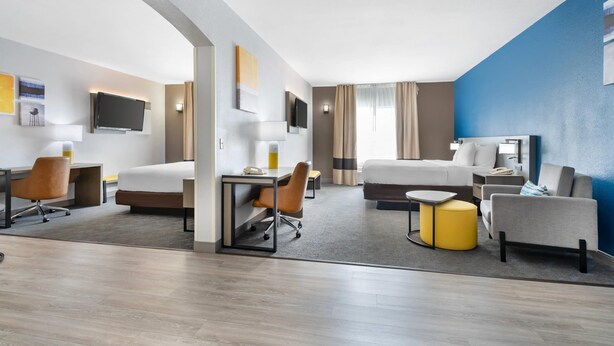 A modern hotel room with a bed, desk, chair, and a small seating area with a yellow ottoman. - Comfort Inn & Suites Sacramento - University Area (Sacramento)