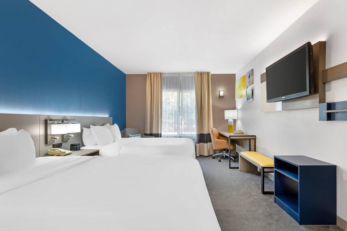 A hotel room with two beds, a desk, a chair, a TV, and a window with curtains.