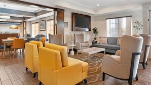 A modern living room with a sofa, armchairs, and a coffee table. There is a television mounted on the wall and a dining area with chairs and a table. - Comfort Inn & Suites Sacramento - University Area (Sacramento)