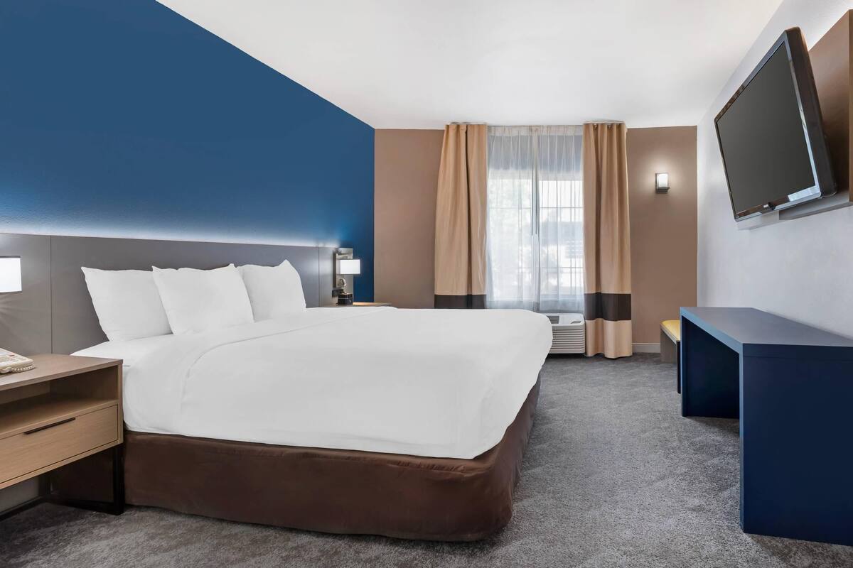 A hotel room with a large bed, a desk, a flat-screen TV, and a window with curtains.