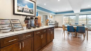 A modern kitchen with a breakfast bar, coffee station, and dining area with blue chairs. - Comfort Inn & Suites Sacramento - University Area (Sacramento)