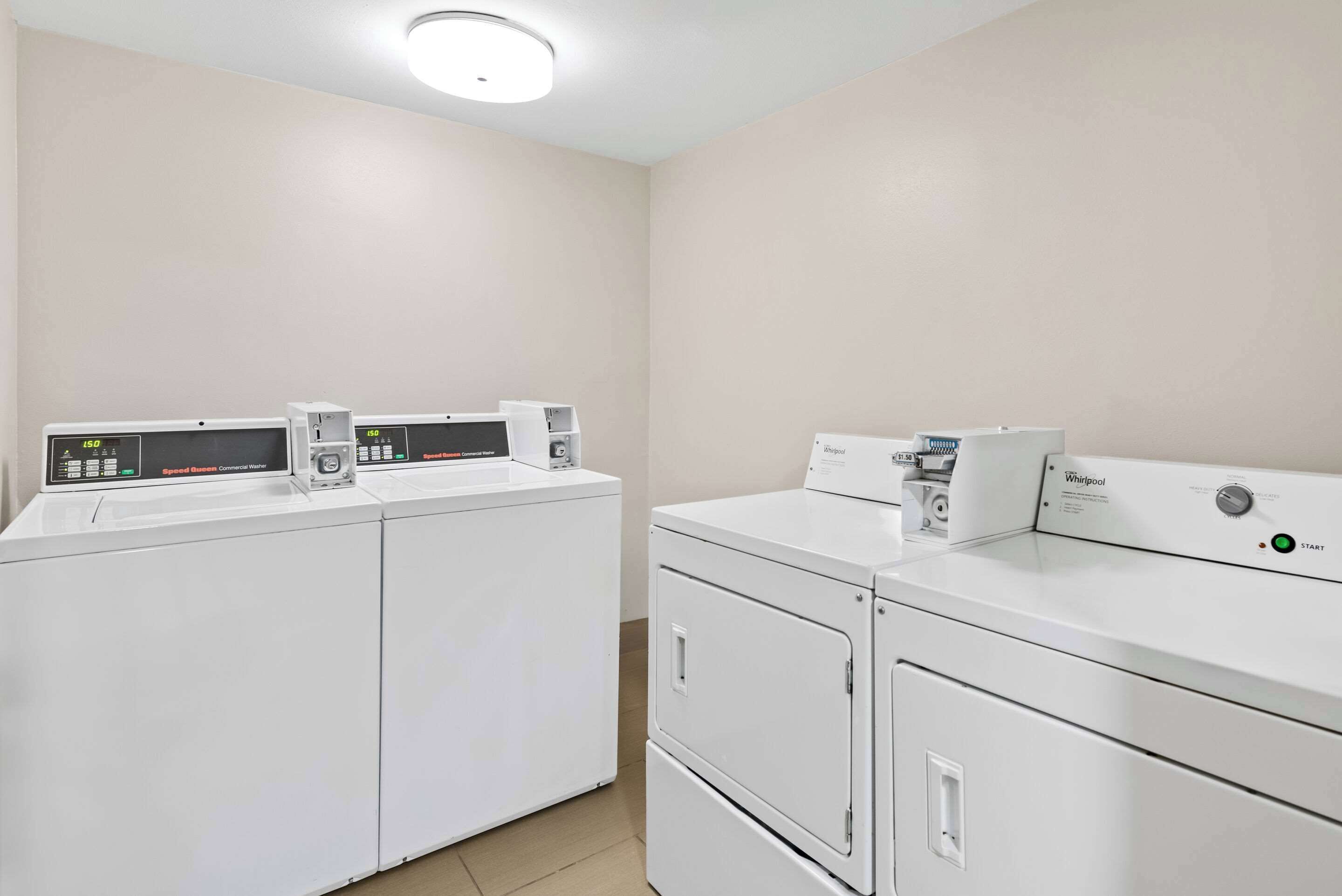 A laundry room with two front-loading washers and dryers, a control panel, and a ceiling light.