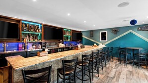 Uma área de bar com um balcão comprido, vários bancos e prateleiras repletas de garrafas.