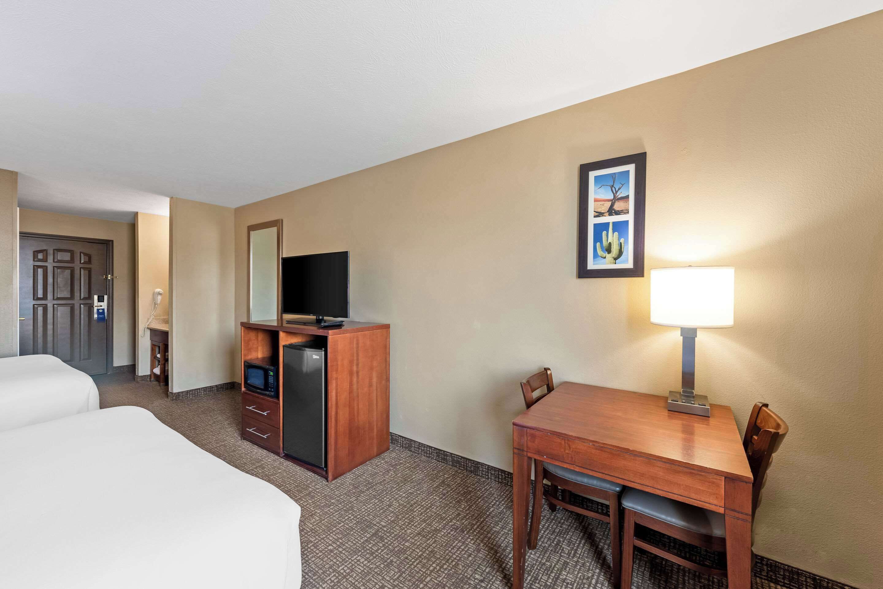 A hotel room with two beds, a desk with a lamp, a television, and a small refrigerator.