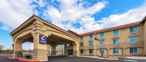 A Comfort Inn & Suites hotel with a covered entrance, multiple balconies, and a clear sky.