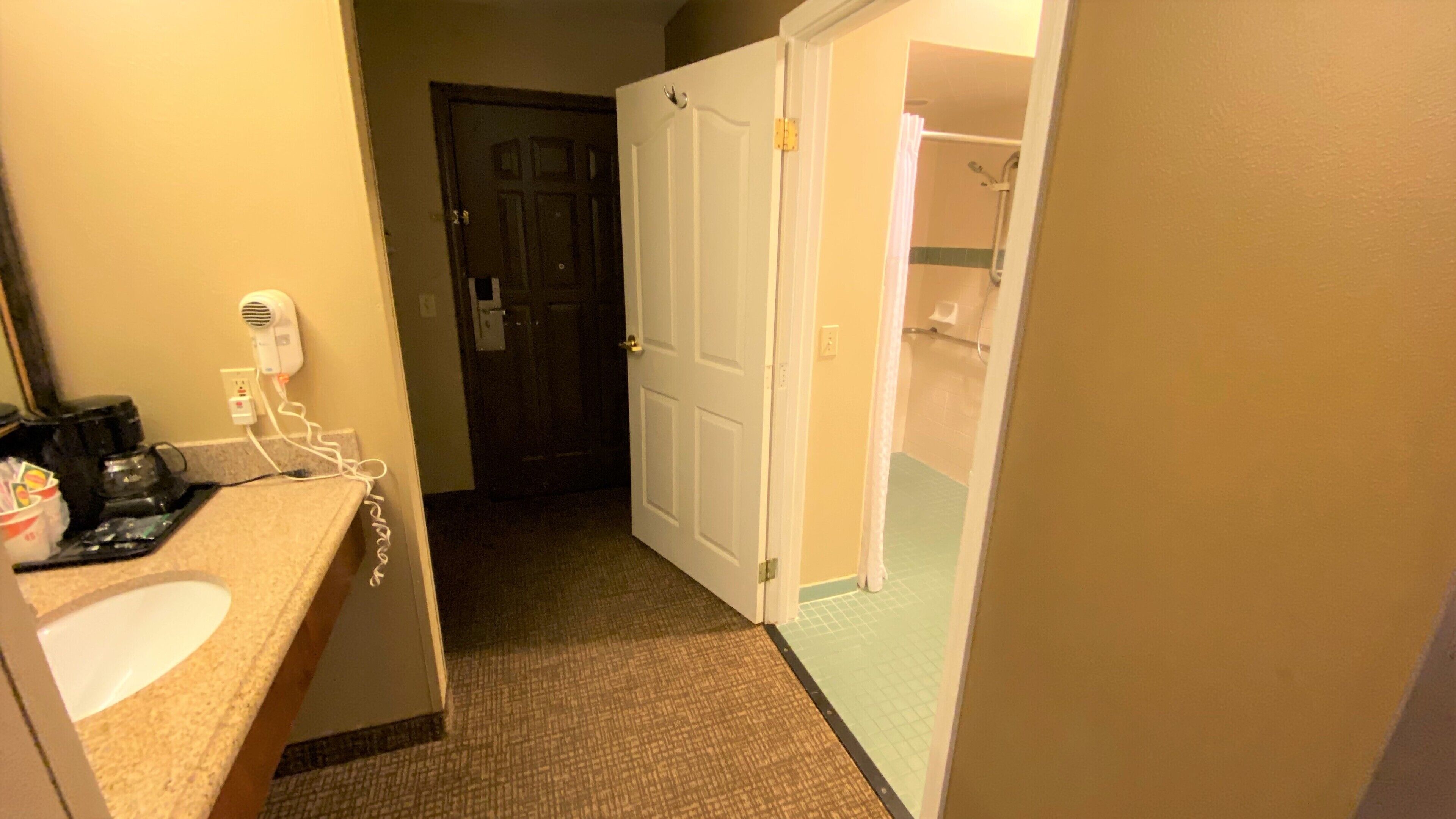 Baño de hotel con lavamanos, secador de pelo y zona de ducha.