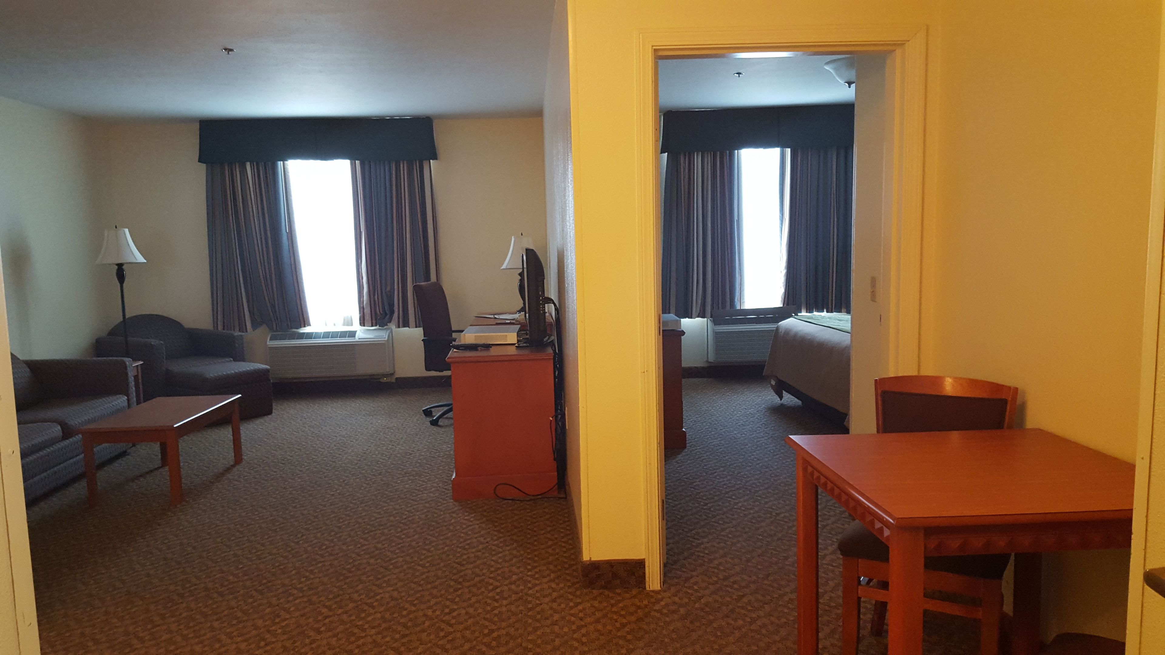 A hotel room with a sofa, a desk, a chair, a bed, and a TV.