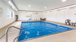 Una piscina interior con agua cristalina, una escalera metálica y un techo con luces empotradas.