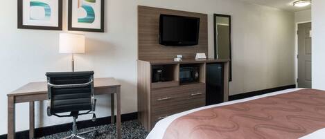 A hotel room with a bed, a desk, a chair, a TV, a dresser, and two framed pictures on the wall.