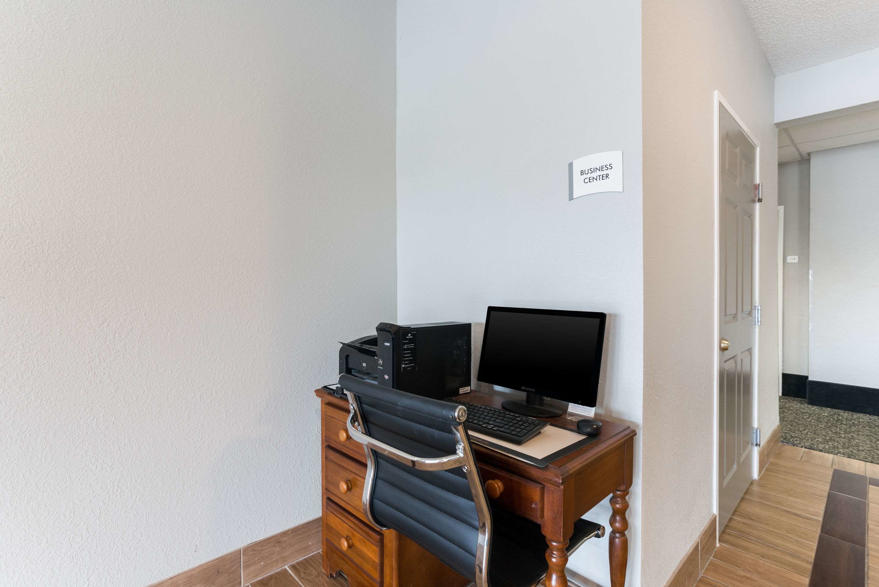 A small office with a desk, chair, computer, and printer. A sign on the wall reads "BUSINESS CENTER".