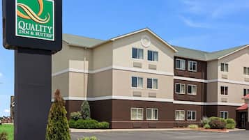 A multi-story hotel with a sign for Quality Inn & Suites, featuring a modern design with a mix of beige and brown exterior colors, large windows, and a parking lot in front.