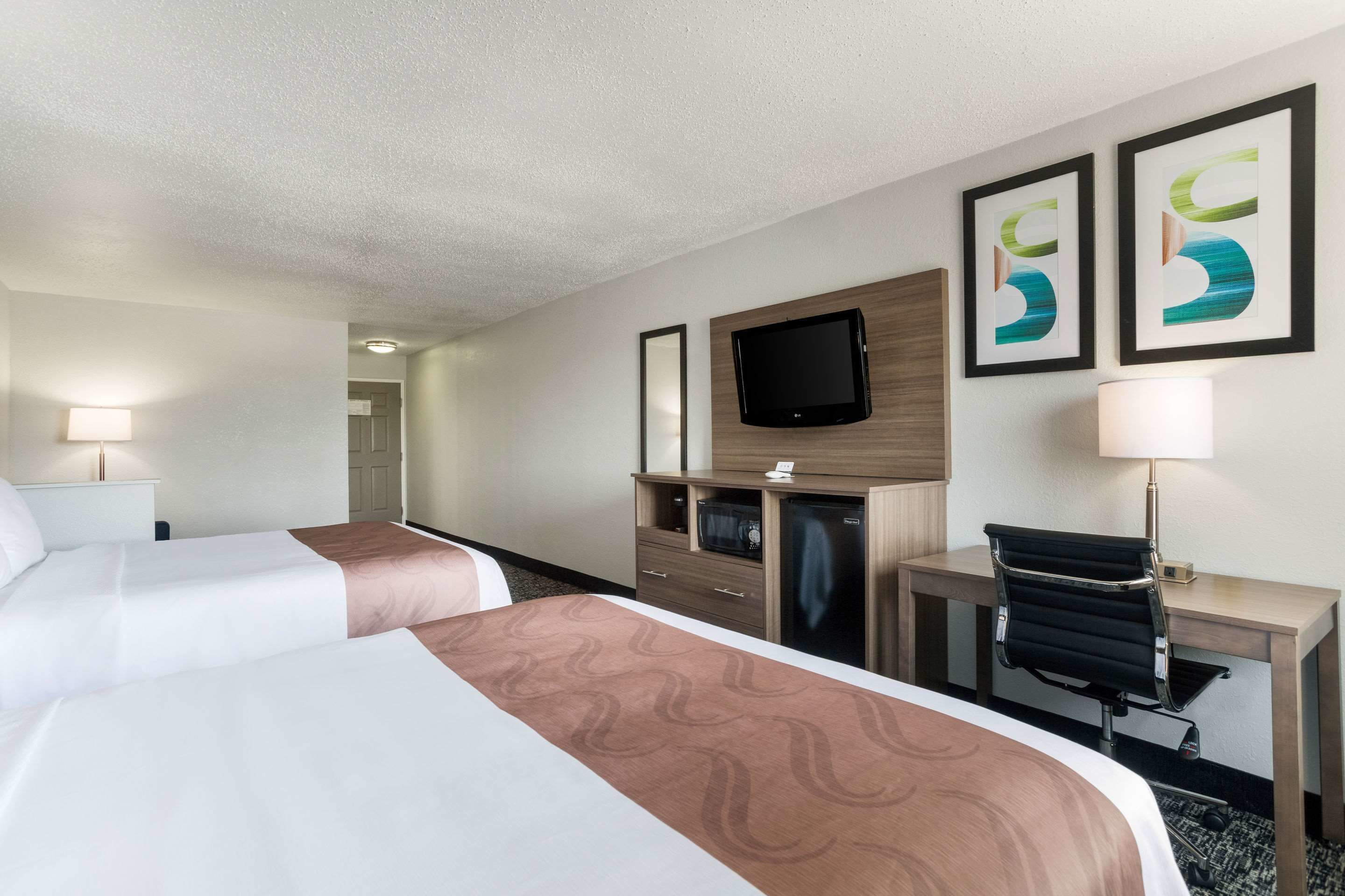 Ett hotellrum med två sängar, ett skrivbord, en stol, en tv och konstverk på väggen.