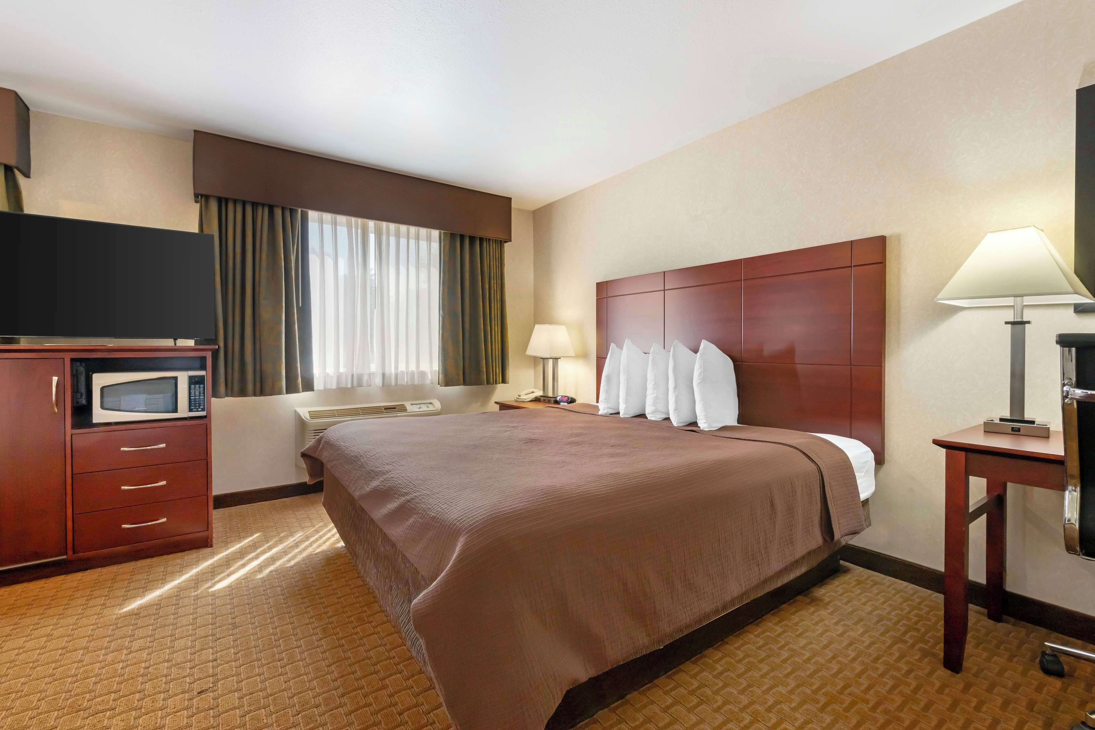 Una habitación de hotel con una cama grande, un televisor de pantalla plana, un microondas, un escritorio con lámpara y una ventana con cortinas.