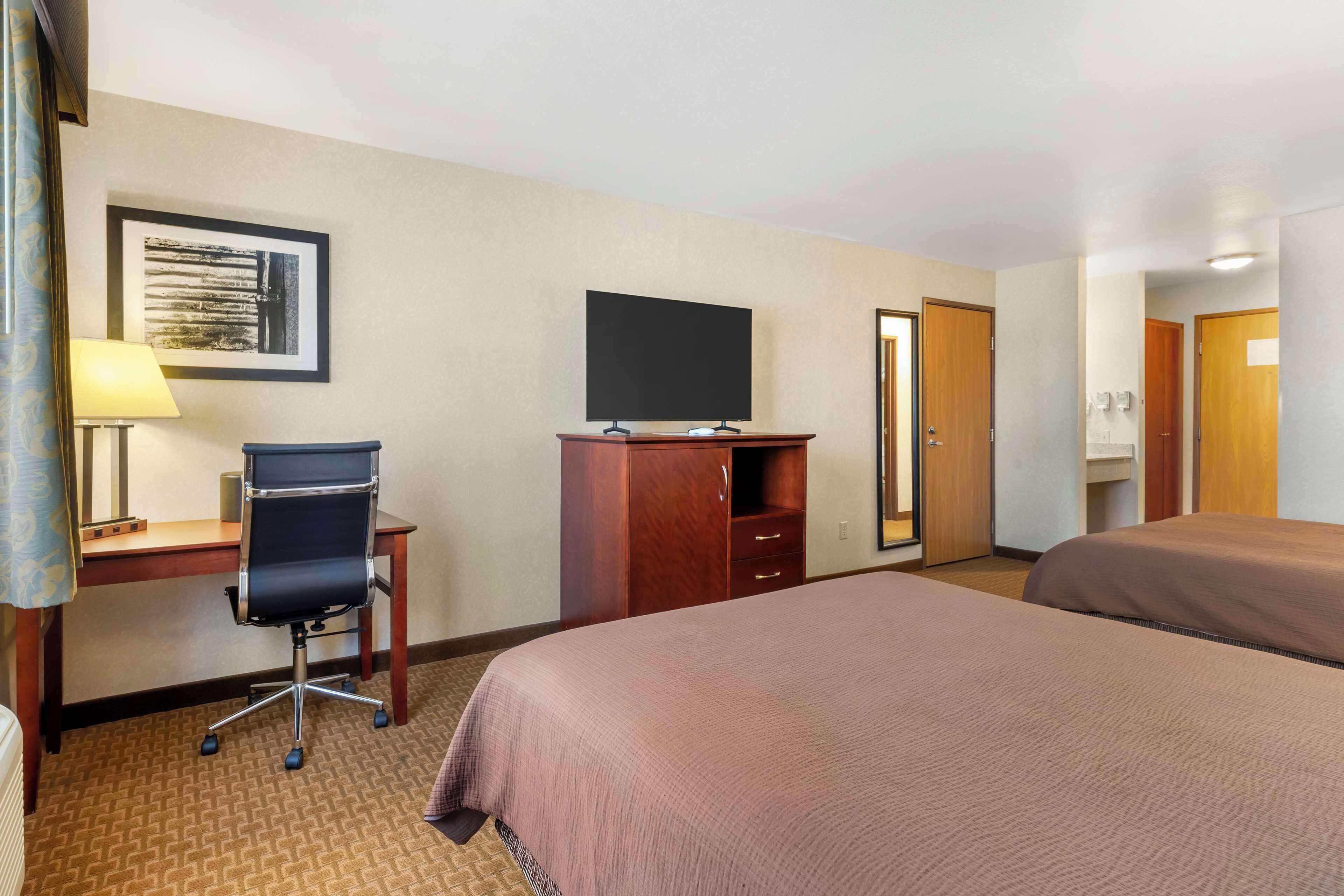 A hotel room with a desk, chair, television, two beds, and a wardrobe.