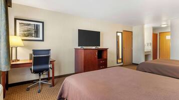 A hotel room with a desk, chair, television, two beds, and a wardrobe.