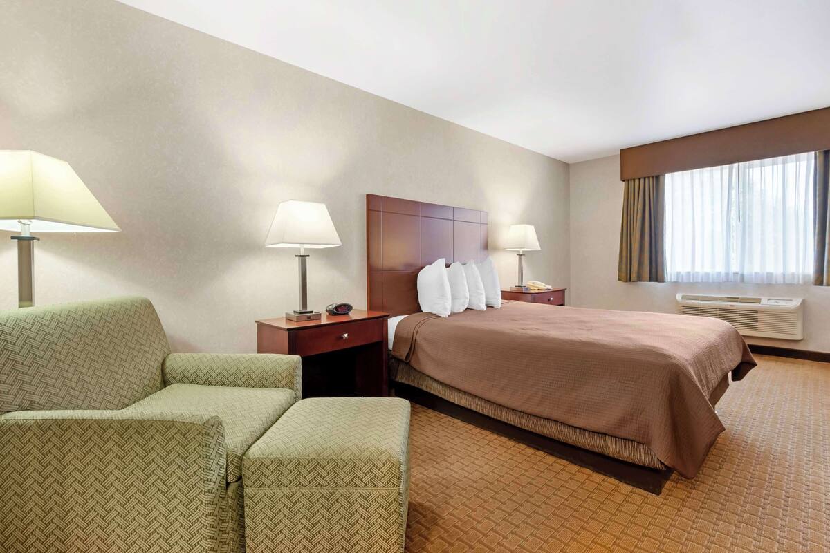 A hotel room with a bed, two bedside tables, a lamp, a sofa, and a window with curtains.